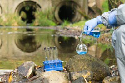 environmental biologist in a protective suit on the shore of a reservoir conducts an express test of river water for pollution
